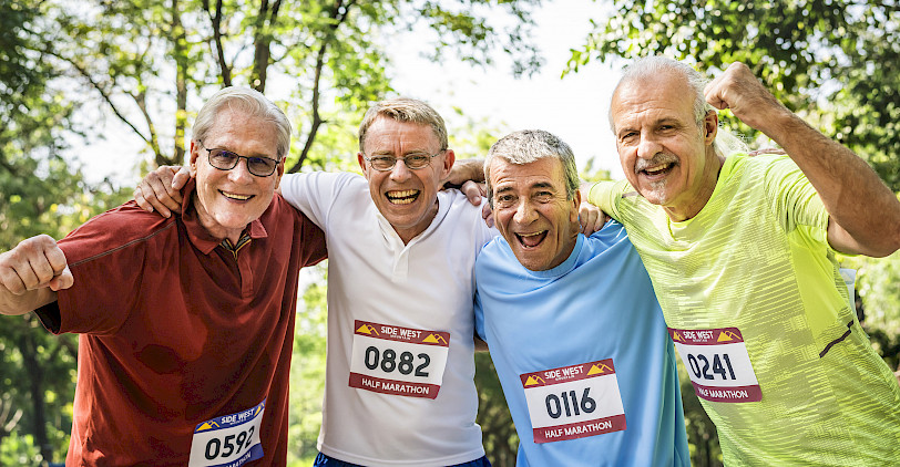 Vier ältere Männer mit Startnummern auf ihren Trikots freuen sich
