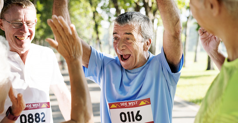 Mehrere ältere Männer mit Startnummern auf ihren Trikots freuen sich