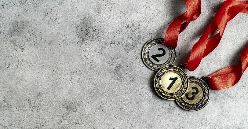 Drei Medaillen mit roten Bändern und den Nummern Eins, Zwei und Drei liegen auf einem grauen Steinhintergund