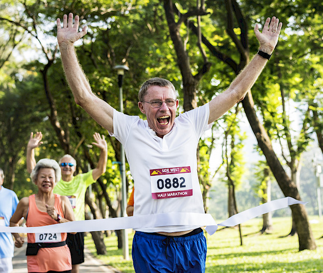 Ein älterer Mann läuft mit gehobenen Armen durch das Zielband