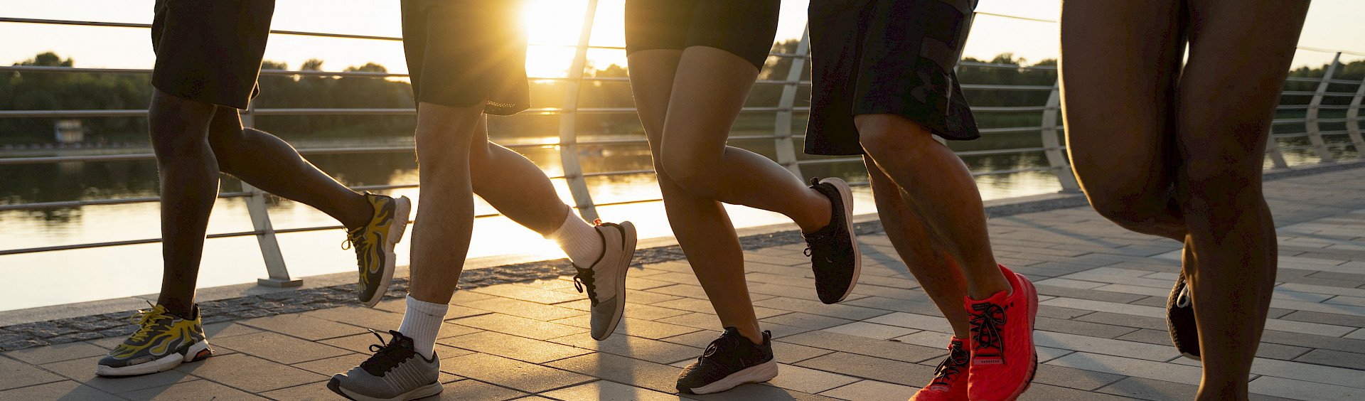 Die Beine von fünf Läufern, die beim Sonnenuntergang am Wasser joggen