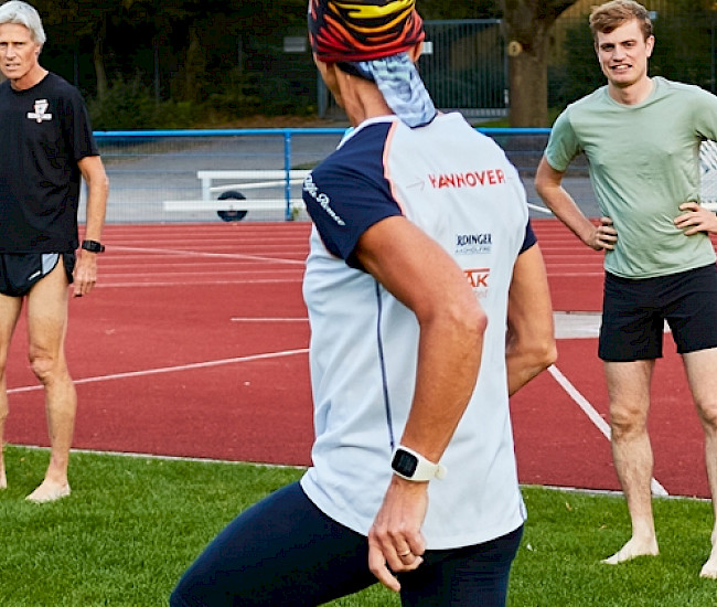 Mehrere Vereinsmitglieder stehen in einer Reihe auf dem Rasen, ein Coach macht Aufwärmübungen vor