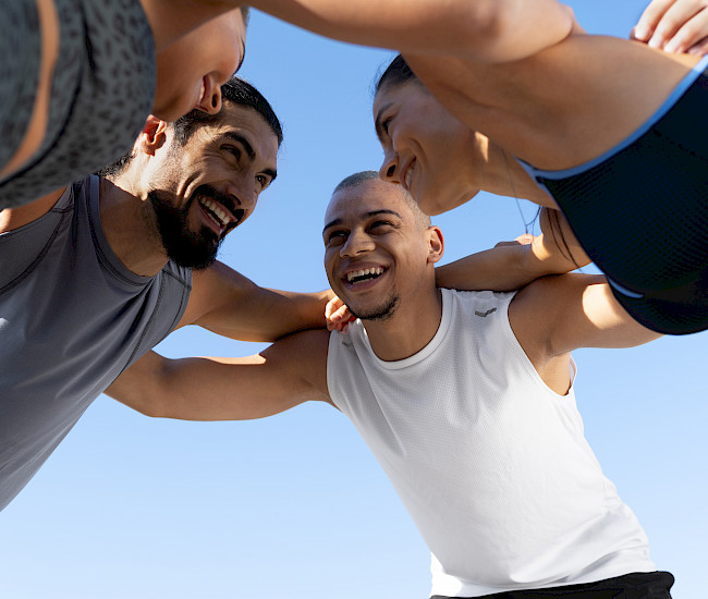 Vier Sportler stecken lachend die Köpfe zusammen